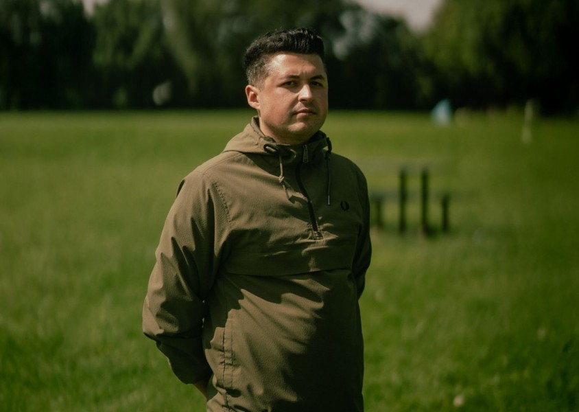 A man with dark hair in a green coat stood in a field x